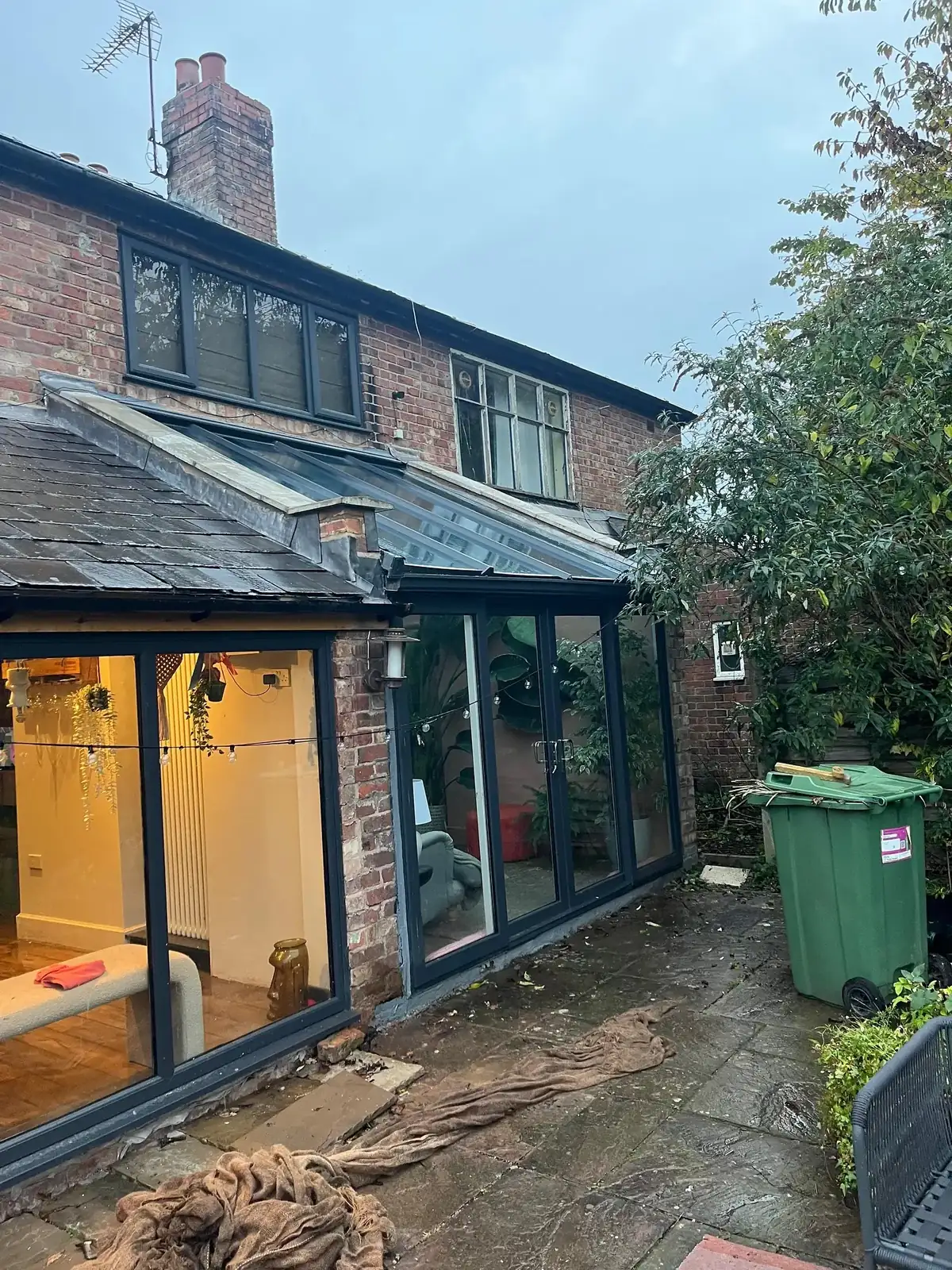 Modern rear extension with full-height dark aluminium glazing, lit from inside at dusk