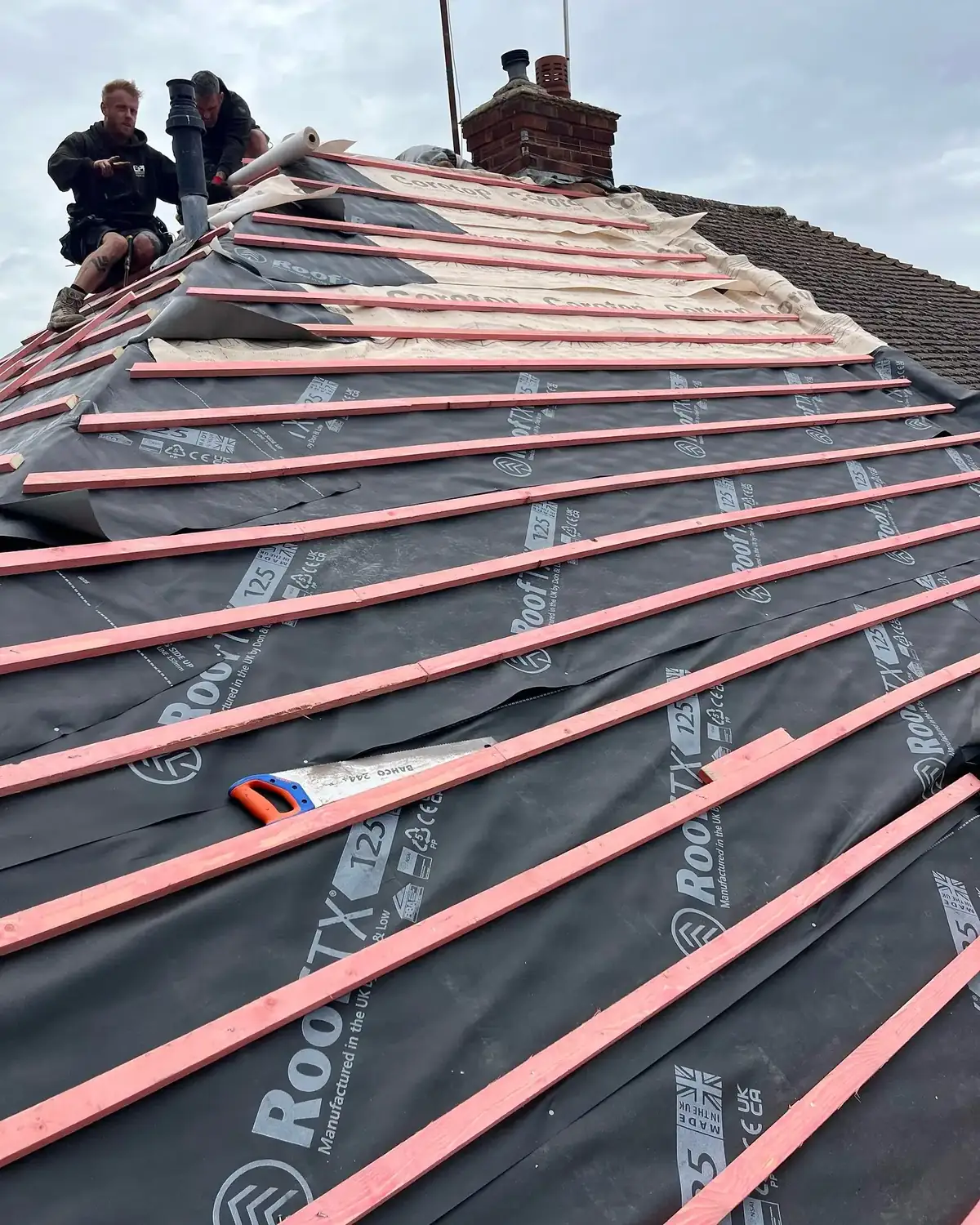 Roofer laying breather membrane and battens across a stripped pitched roof